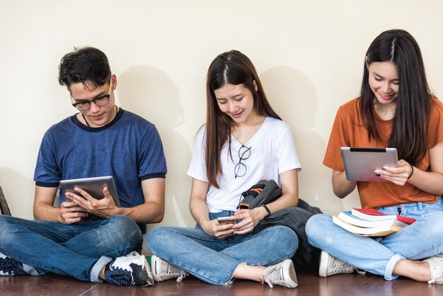 Jóvenes y amigas compañeras de clase sentadas usando tecnología de teléfono móvil y tablet en la universidad juntos