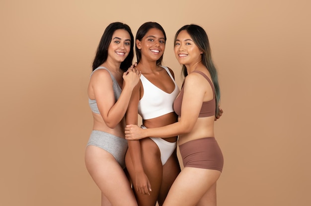 Foto jóvenes amigas internacionales positivas en ropa interior diferente posando aisladas en beige