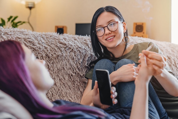 Jóvenes amigas sonrientes fumando marihuana en casa mientras se relajan en el sofá