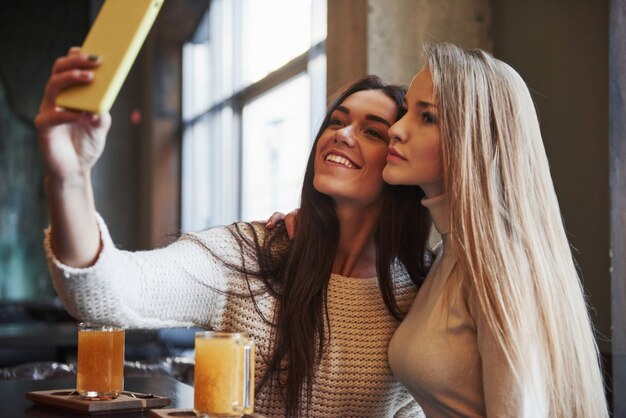 Jóvenes amigas toman selfie en el restaurante con dos bebidas amarillas en la mesa