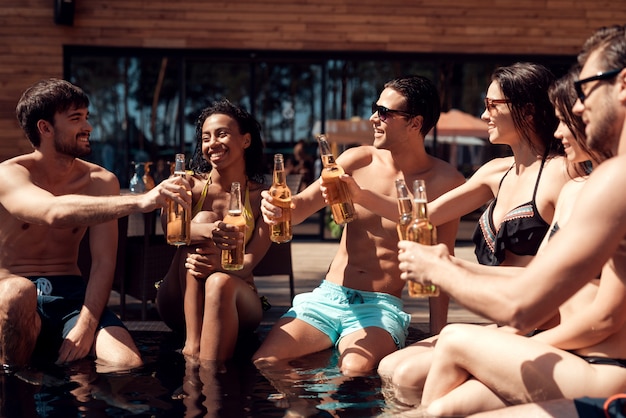 Jóvenes amigos con bebidas alcohólicas en la piscina