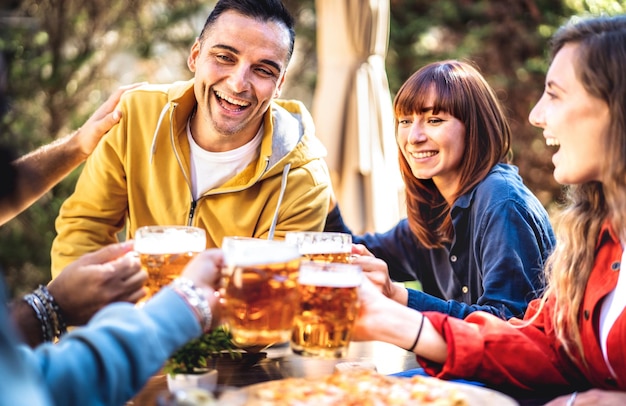 Jóvenes amigos bebiendo y brindando pintas de cerveza en el jardín del bar de la cervecería afuera Concepto de estilo de vida de bebidas con chicos y chicas divirtiéndose juntos en la hora feliz Filtro brillante con enfoque en el hombre izquierdo