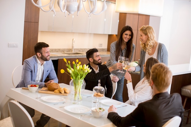 Jóvenes amigos cenando en casa y brindando con vino blanco.