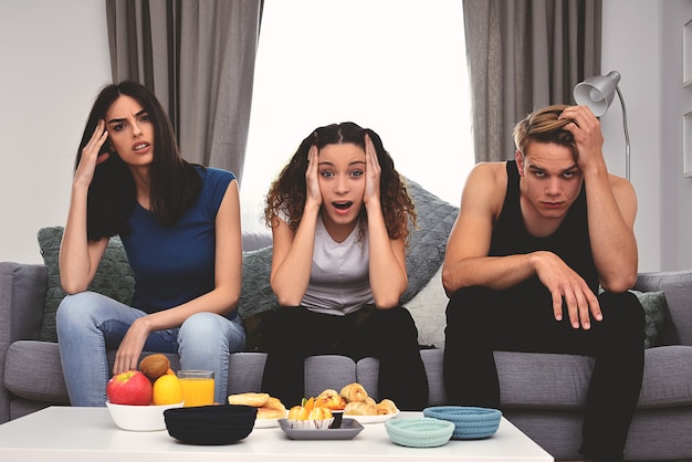 Jóvenes amigos haciendo emociones mientras ven la televisión en casa juntos