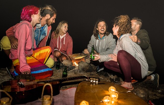 Jóvenes amigos hippies divirtiéndose juntos en la fiesta de camping en la playa con barbacoa nocturna