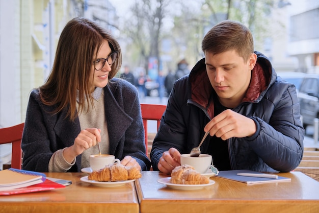 Jóvenes amigos hombres y mujeres estudiantes sentados en la cafetería al aire libre