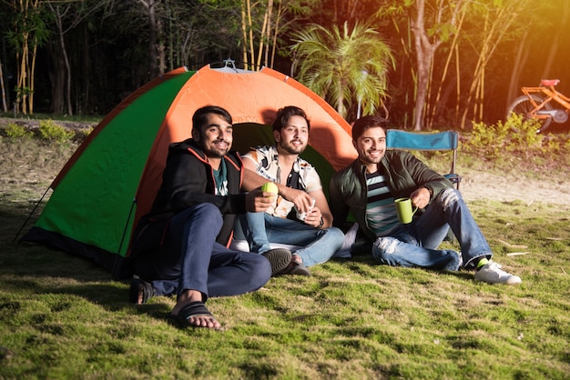 Jóvenes amigos indios asiáticos pasar un buen rato en un viaje de campamento de vacaciones relajantes con divertidas tiendas de campaña al aire libre