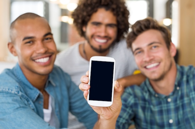 Jóvenes amigos que muestran la pantalla en negro del teléfono inteligente en la cámara