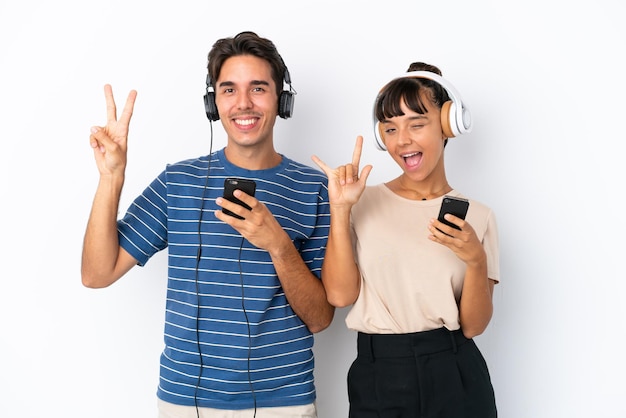 Jóvenes amigos de raza mixta aislados de fondo blanco escuchando música con un móvil haciendo gestos de rock