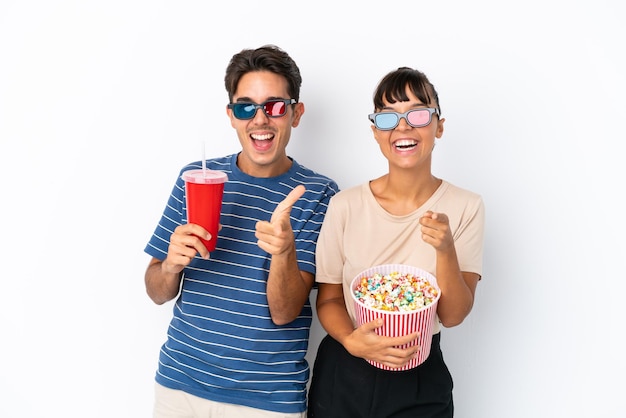 Jóvenes amigos de raza mixta aislados de fondo blanco con gafas 3d y sosteniendo un gran cubo de palomitas de maíz mientras apuntan al frente
