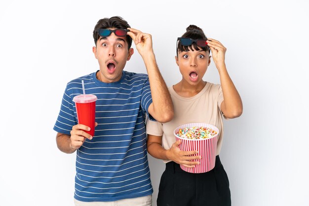 Jóvenes amigos de raza mixta aislados de fondo blanco sorprendidos con gafas 3d y sosteniendo un gran cubo de palomitas de maíz