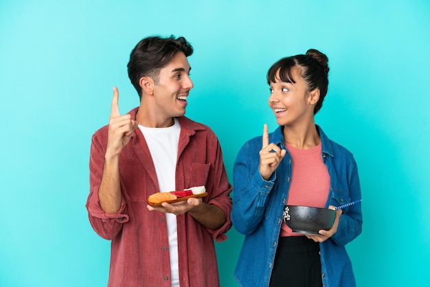 Jóvenes amigos de raza mixta sosteniendo sashimi y ramen aislados sobre fondo azul con la intención de darse cuenta de la solución mientras levantan un dedo