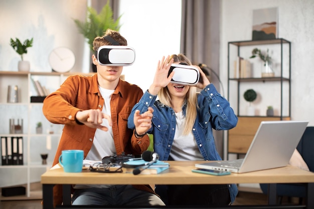 Jóvenes amigos sentados en la mesa con auriculares VR y disfrutando de la realidad 3D