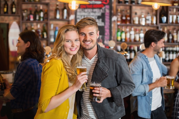 Jóvenes amigos sosteniendo vasos de cerveza en el pub