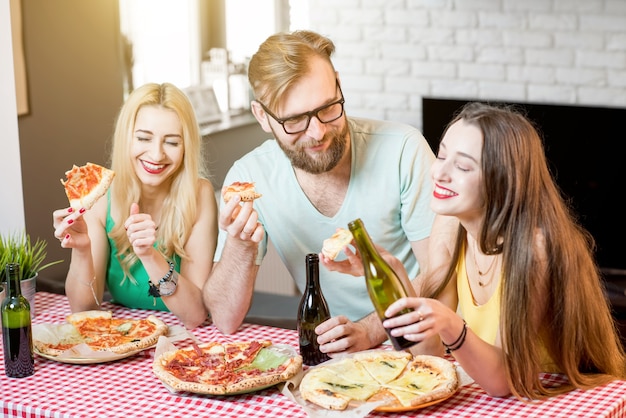 Jóvenes amigos vestidos casualmente con camisetas coloridas almorzando con pizza y cerveza en casa