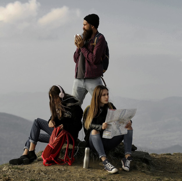 Jóvenes amigos viajeros hipster hombre barbudo y dos mujeres chicas guapas con mapa explorar ruta al aire libre en la cima de la montaña en el cielo brumoso