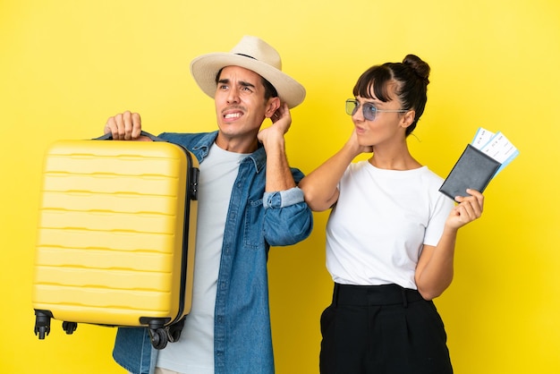 Jóvenes amigos viajeros que sostienen una maleta y un pasaporte aislados en un fondo amarillo que tienen dudas mientras se rascan la cabeza