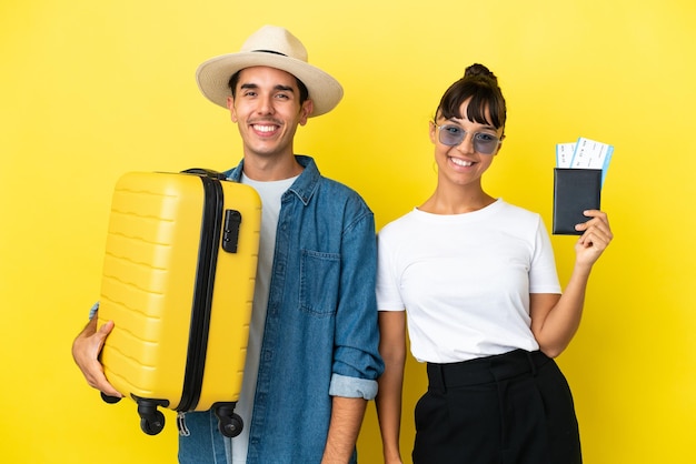 Jóvenes amigos viajeros sosteniendo una maleta y un pasaporte aislados en un fondo amarillo posando con los brazos en la cadera y sonriendo