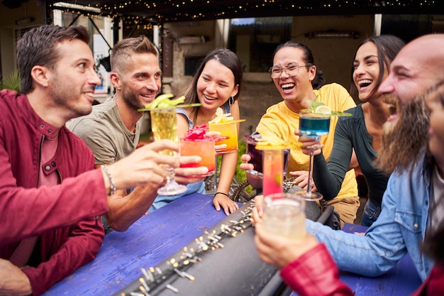 Jóvenes animados y divirtiéndose grupo de amigos felices bebiendo y brindando cócteles en la cervecería