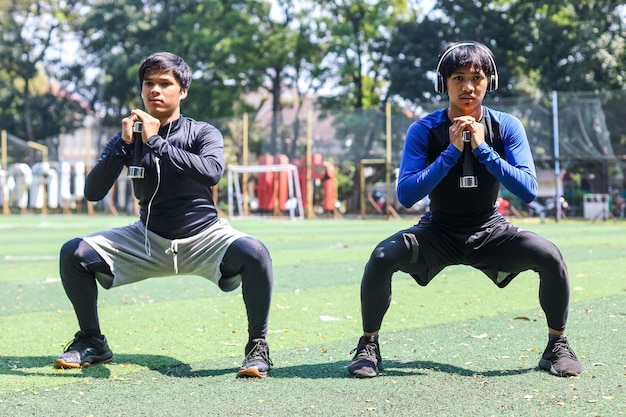 Jóvenes asiáticos haciendo sentadillas juntos mientras hacen ejercicio al aire libre en un prado en un parque soleado