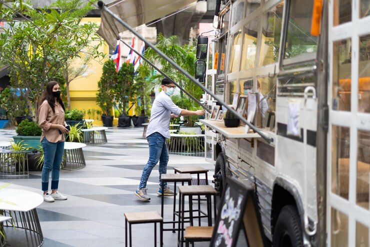 Jóvenes asiáticos con máscaras faciales hacen fila para comprar café en un patio multiusos en la ciudad