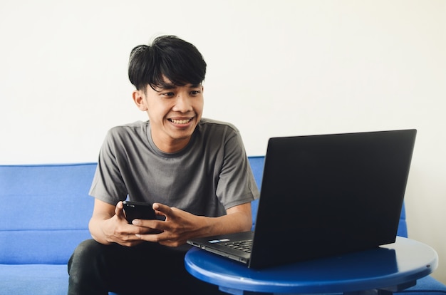 Jóvenes asiáticos sentados en el sofá frente a la computadora portátil usando un teléfono celular