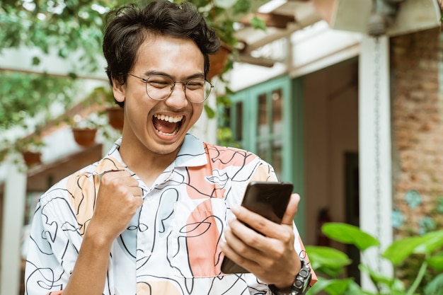 Jóvenes asiáticos sosteniendo y mirando teléfonos celulares están muy felices