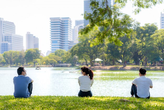 Jóvenes asiáticos de tres hombres y mujeres hablando y relajándose con sus amigos y usando una máscara a una distancia de 6 pies de distancia protegen contra los virus COVID-19 para el distanciamiento social