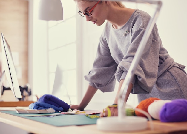 Jóvenes y atractivas diseñadoras de moda apoyándose en el escritorio de la oficina trabajando con una computadora portátil