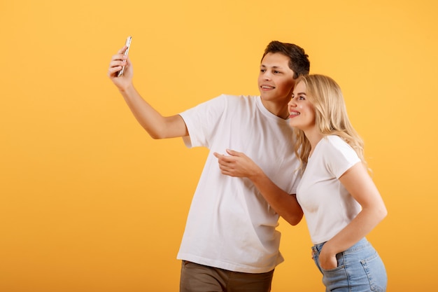 Jóvenes y atractivos amigos sobre un fondo naranja tomando selfies