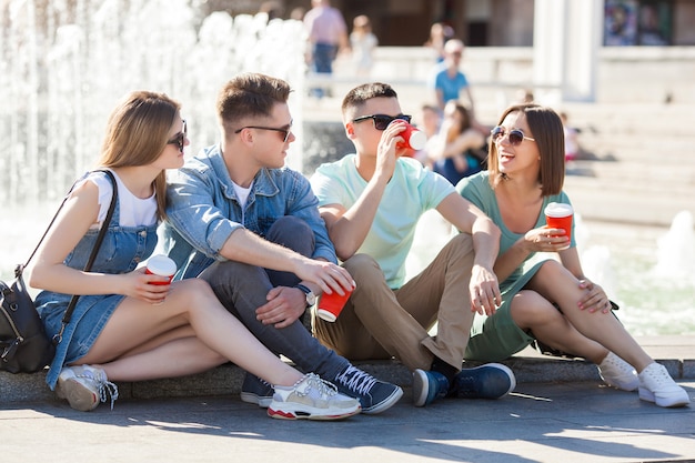 Jóvenes atractivos que se divierten juntos al aire libre. Gente bebiendo café y sonriendo. Grupo de amigos caminando juntos.