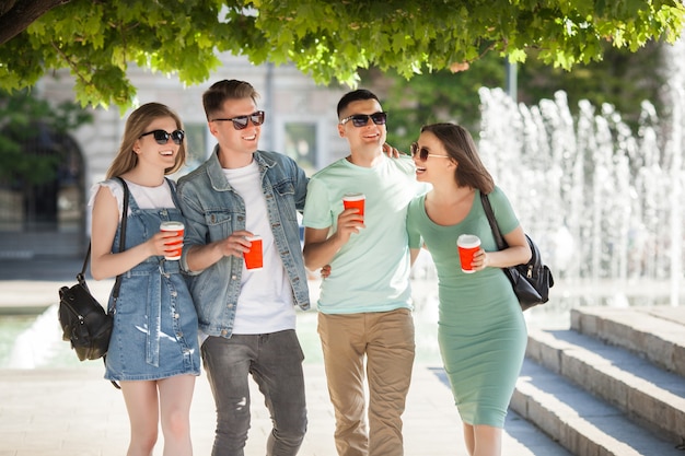 Jóvenes atractivos que se divierten juntos al aire libre. Gente bebiendo café y sonriendo. Grupo de amigos caminando juntos.