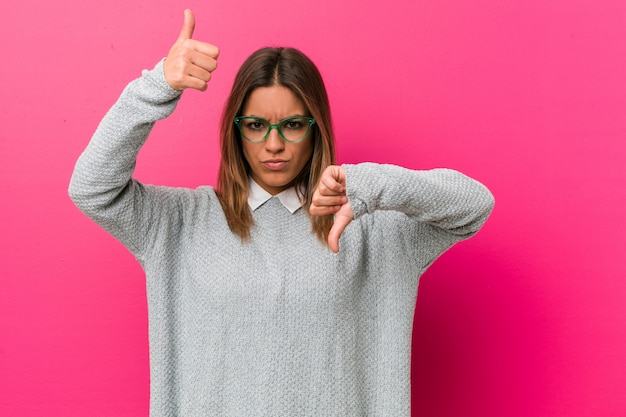 Jóvenes auténticos carismáticos personas reales mujer contra una pared mostrando los pulgares hacia arriba y hacia abajo, difícil elegir el concepto