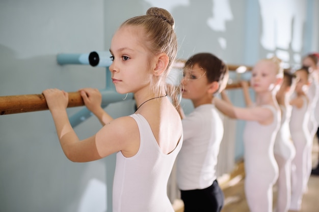 Jóvenes bailarines en el estudio de ballet. Los jóvenes bailarines realizan ejercicios de gimnasia en el ballet o la barra mientras hacen calentamiento en el aula.