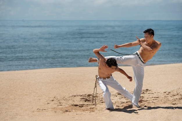 Jóvenes sin camisa practicando capoeira juntos en la playa