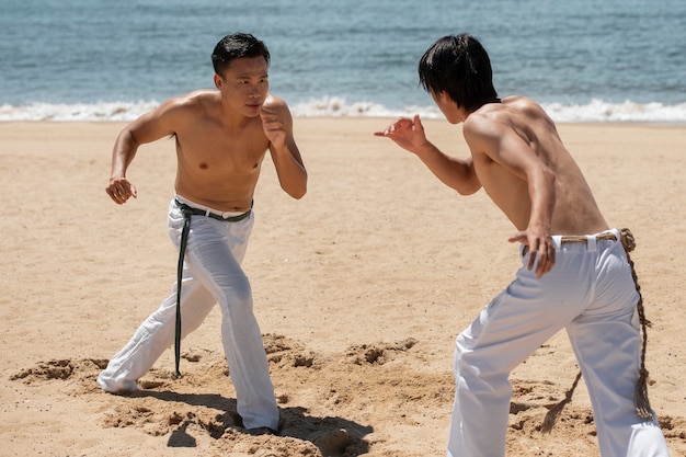 Jóvenes sin camisa practicando capoeira juntos en la playa