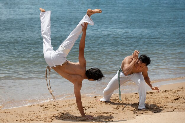 Foto jóvenes sin camisa practicando capoeira juntos en la playa