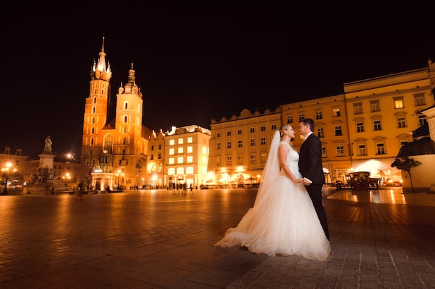 Jóvenes casados ​​enfrentados sonriendo amorosamente posando en la ciudad