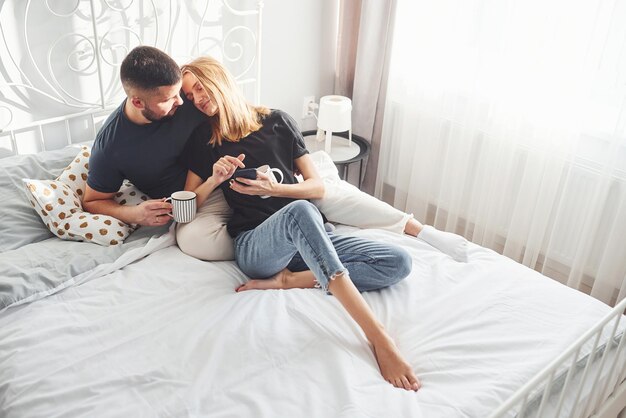 Los jóvenes casados con una taza de bebida tienen tiempo libre juntos en el dormitorio durante el día.