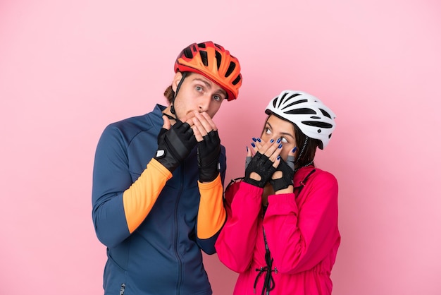 Jóvenes ciclistas caucásicos aislados de fondo rosa cubriéndose la boca con las manos por decir algo inapropiado