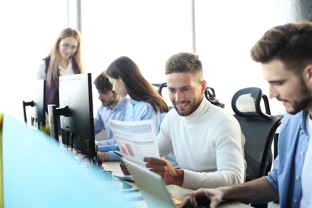 Jóvenes colegas modernos en ropa casual elegante trabajando juntos mientras pasan tiempo en la oficina creativa.