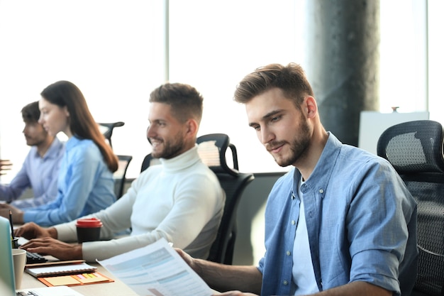 Jóvenes colegas modernos en ropa casual elegante trabajando juntos mientras pasan tiempo en la oficina creativa.