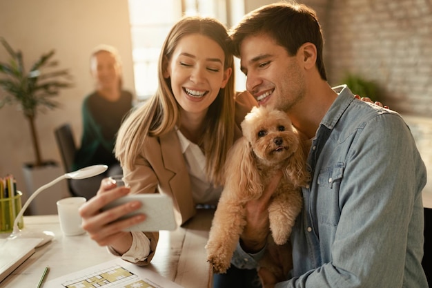 Jóvenes colegas de negocios divirtiéndose mientras toman selfie con un perro en la oficina