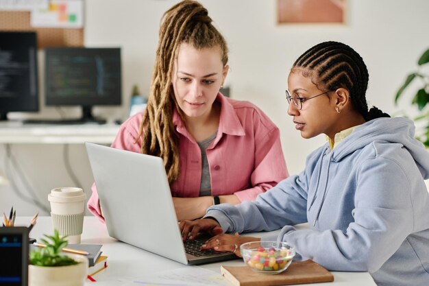 Jóvenes colegas que desarrollan un nuevo software en equipo se sientan a la mesa y trabajan en una computadora portátil