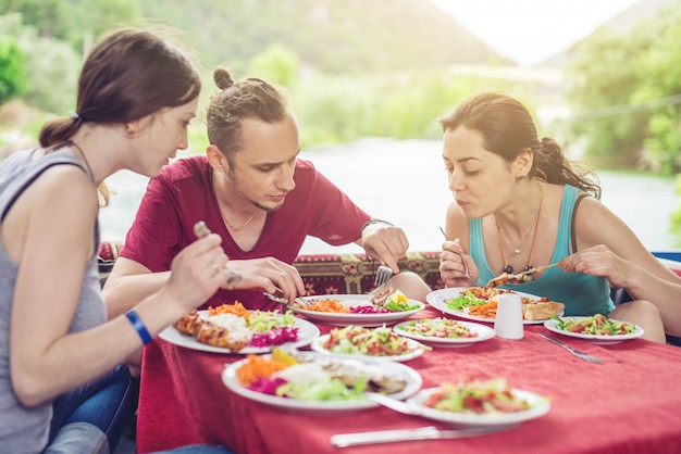 Los jóvenes comen verduras y pescado al aire libre en un acogedor restaurante en el agua