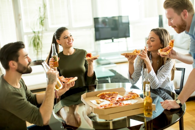 Foto jóvenes comiendo pizza y bebiendo sidra en la habitación