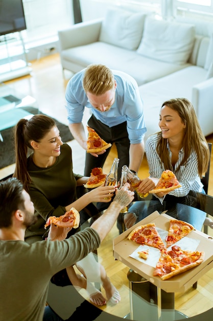 Foto jóvenes comiendo pizza y bebiendo sidra en el interior moderno