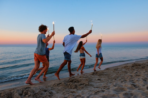 Los jóvenes corren por la playa con velas brillantes en las manos