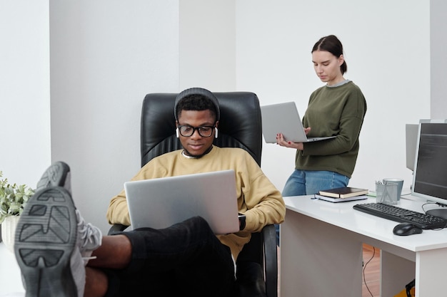 Jóvenes desarrolladores interculturales con laptops trabajando individualmente en la oficina