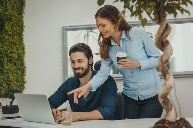 Jóvenes diseñadores exitosos están trabajando en una computadora portátil y hablando de proyectos en la oficina durante el descanso para tomar café.